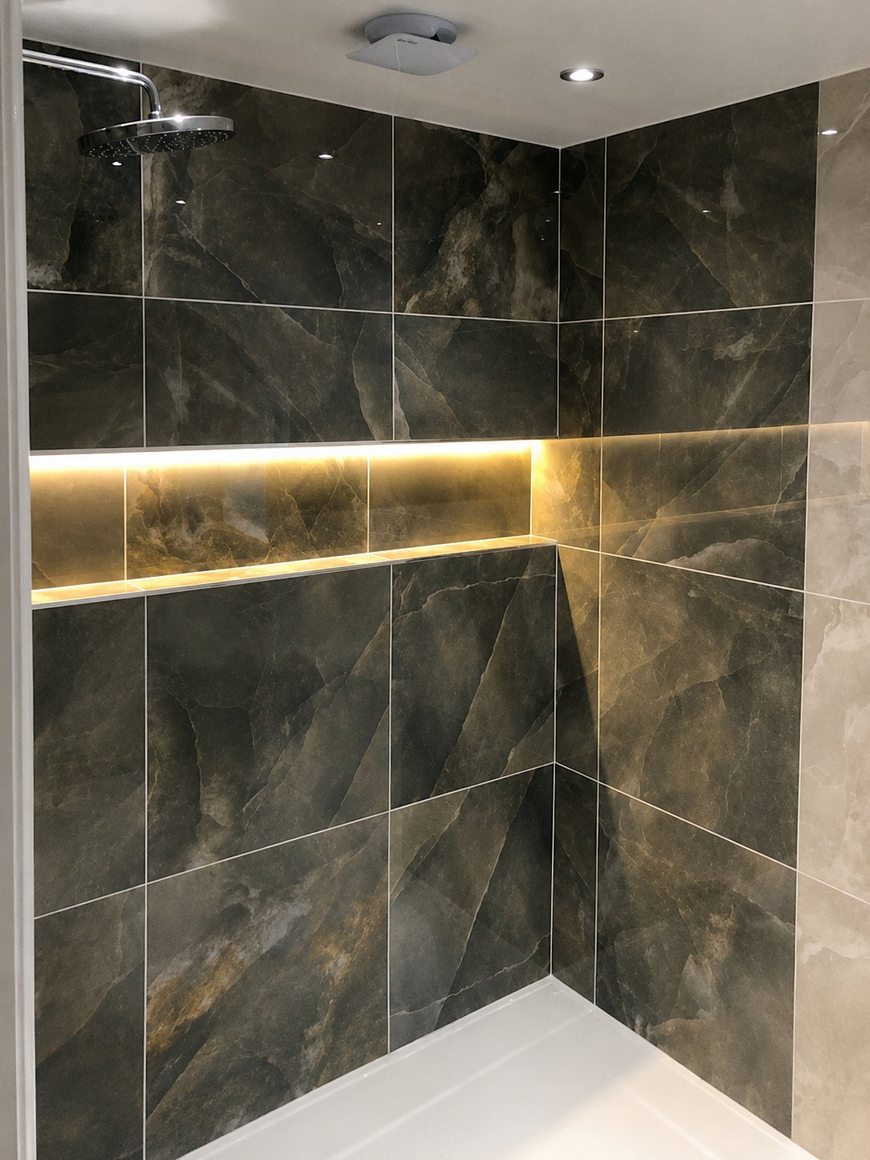 Finished walk-in shower by Andrade Renovations — dark marble tiling, brass detail and backlit LED niche